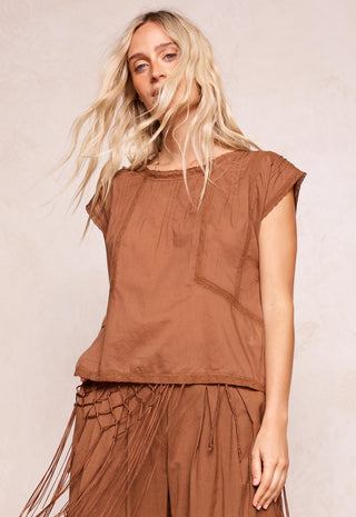 a-woman-modeling-a-brown-short-sleeve-top-and-matching-brown-fringed-skirt-against-a-light-beige-textured-background