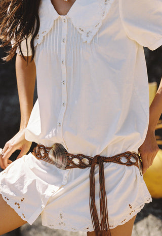 A close-up of a person wearing a white short-sleeve blouse and matching white shorts with eyelet lace trim, styled with a brown woven belt.