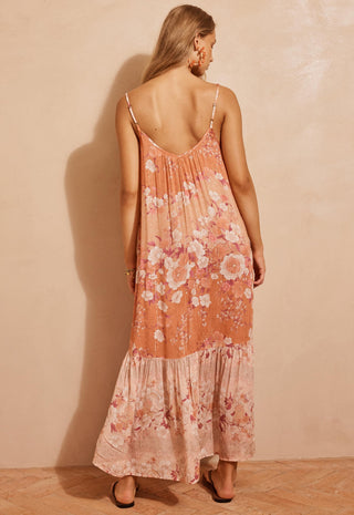 a-woman-wearing-a-peach-and-pink-floral-maxi-dress-with-spaghetti-straps-shown-from-the-back-against-a-textured-beige-wall