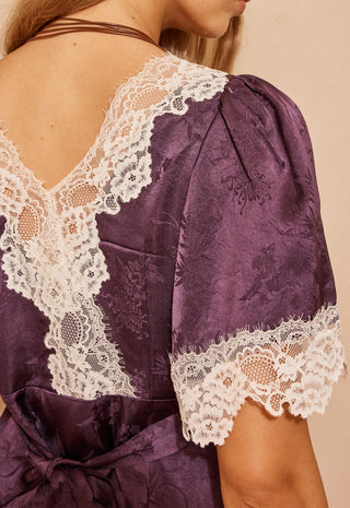 close-up-of-the-back-of-a-purple-satin-dress-with-white-lace-trim-on-the-shoulders-and-sleeves-worn-by-a-model