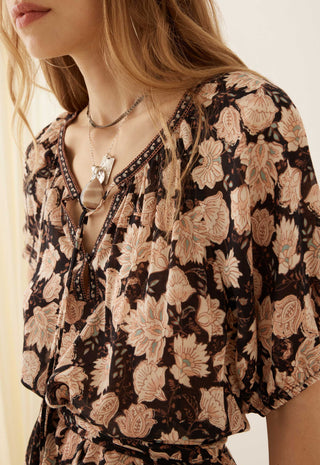 A close-up of a woman wearing a brown and beige floral print blouse with a V-neckline and layered necklaces.