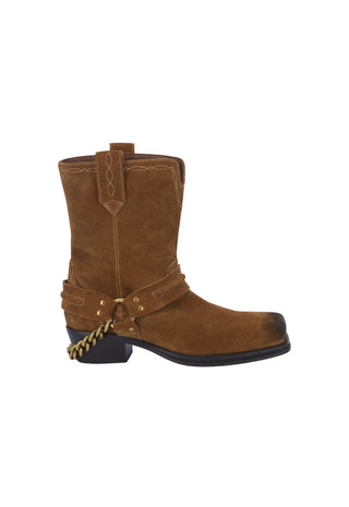 A black ankle boot with a chunky block heel, featuring a black faux-leather upper, a black suede side panel, a black elastic side strap with a gold-tone eyelet, and a small gold logo on the side.