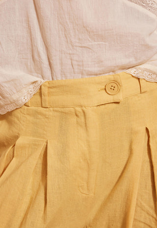 Close-up of a yellow linen pleated skirt paired with a cream-colored lace-trimmed blouse.